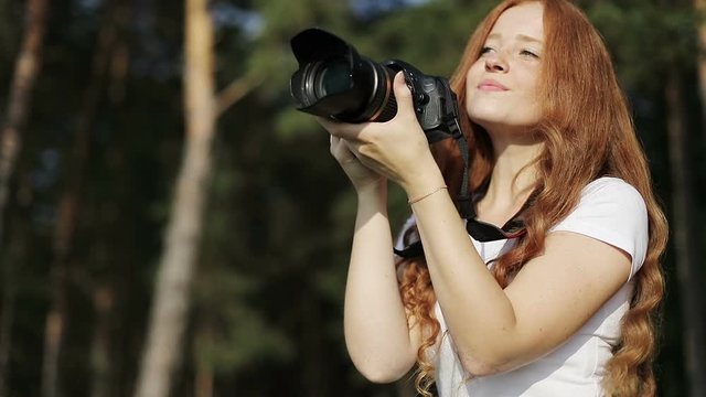 Sun-kissed redhead girl with photo-camera is smiling and looking at the sunset.