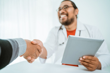 portrait of smiling doctor shaking hand with patient in his office