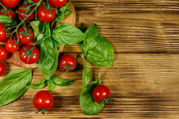 Fresh cherry tomatoes with green basil leaves on a wooden table. Top view