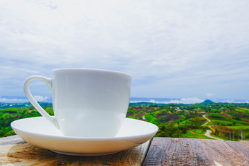 White hot coffee mugs placed on a wooden floor with green fresh mountain and morning fog as background