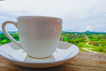 White hot coffee mugs placed on a wooden floor with green fresh mountain and morning fog as background