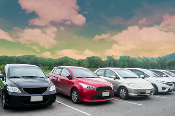 Fototapeta na wymiar Cars parking in asphalt parking lot in a row with trees, colorful cloudy sky background in a park