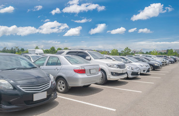 Car parking in large asphalt parking lot with trees, white cloud and blue sky background © merrymuuu