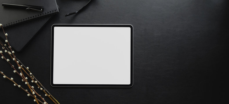 Overhead shot of blank screen tablet on black desk in dark luxury workspace