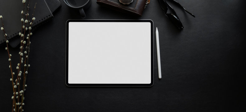 Top view of blank screen digital tablet on blank desk in dark luxury workspace