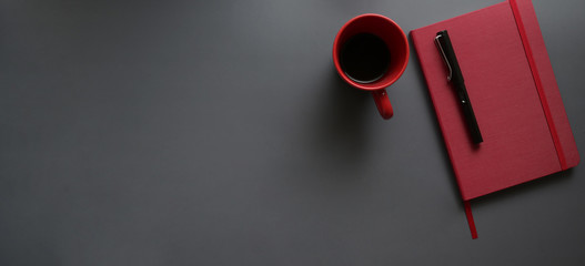 Top view of dark modern workplace with red notebook and red coffee cup on dark grey desk