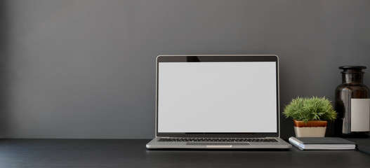 Open blank screen laptop computer in dark trendy workplace with copy space