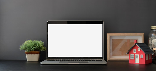 Blank screen laptop computer in dark trendy workplace with office supplies