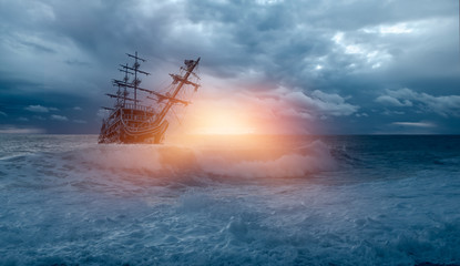 Obraz premium Sailing old ship in storm sea against heavy sunset clouds