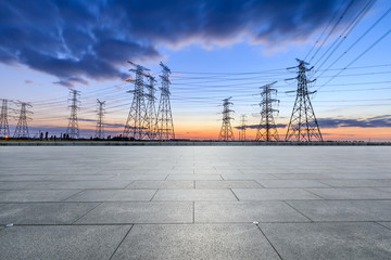 Empty square floor and high voltage electricity tower landscape at sunset.