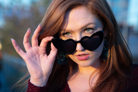 Red head young woman head and hand with heart shapped sunglasses eyes looking at camera