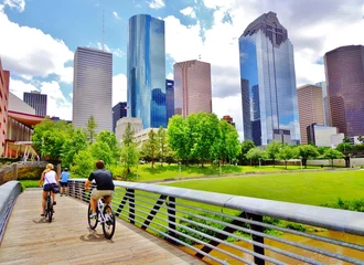 Bicyclists cross wooden bridge in Buffalo Bayou Park, with a beautiful view of downtown Houston (skyline / skyscrapers) in background on a summer day - Houston, Texas, USA 
