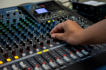  The sound mixer with hand is adjusting sound. Hand pressing the button on the audio mixer.
