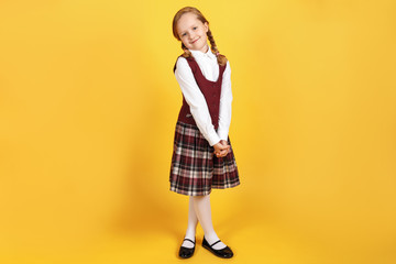 Full-length schoolgirl in uniform on a yellow background. Cute little girl is smiling and looking...
