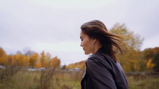 A girl in a black leather jacket is walking in the cool, windy weather outside. Her hair develops in the wind