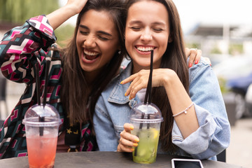 Hipster girlfriends drink cocktail in urban city background