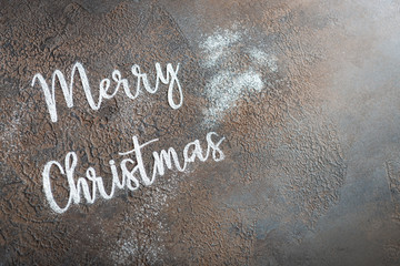 Fototapeta na wymiar Christmas background. Merry christmas lettering made with sugar powder on gray table. Top view, copy space