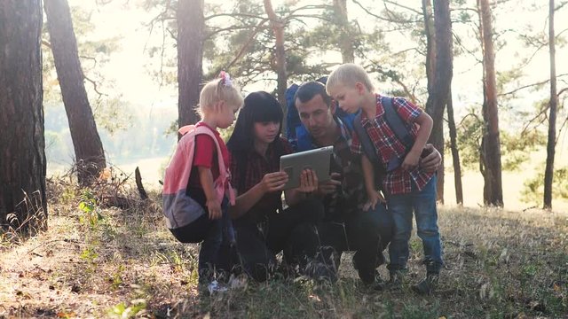happy family navigation tourists teamwork slow motion video concept. mom dad son and daughter hiking in the forest looking for a way on a digital tablet. group of people hikers with backpacks. happy
