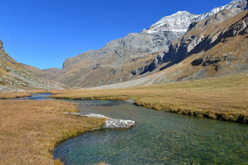 Fototapeta na wymiar clear water of a river crossing alpine mountain with snowy peaks