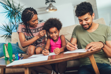 Mom and dad drawing with their daughter. African american family spending time together at home.