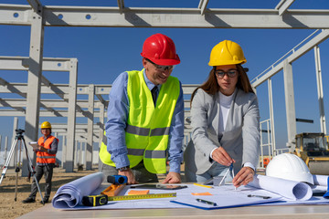 Young Female Architect and Site Supervisor Checking the Construction Blueprint on Construction Site