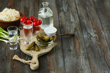 Vodka with salted vegetables on wooden background. Alcohol pure craft drink and traditional snack, tomatos, cabbage, cucumbers. Negative space. Celebrating food and delicious.