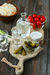 Vodka with salted vegetables on wooden background. Alcohol pure craft drink and traditional snack, tomatos, cabbage, cucumbers. Negative space. Celebrating food and delicious.