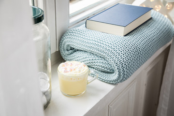 Heiße, weiße Trinkschokolade mit Sahne und Marshmellows Fensterbank mit gemütlicher Wolldecke und Buch am entspannten Wochenende