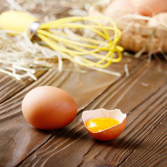 Raw organic brown chicken broken eggs with yolk wicker basket and whisk on kitchen wooden table