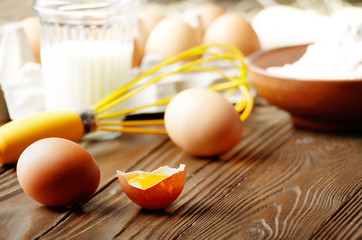 Raw organic brown chicken broken eggs with yolk flour milk and whisk on kitchen wooden table