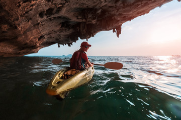 Woman paddles kayak in the tropical sea at sunset and passes the limestone mountains with...
