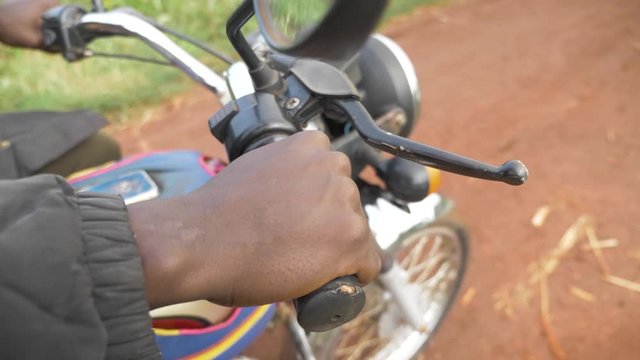 Close up of a African mans hand revving the throttle of a motor bike in rural Africa.