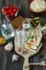 Vodka with lard, salted vegetables on wooden background. Alcohol pure craft drink and traditional...