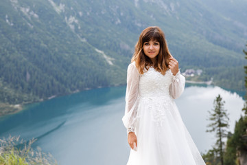 Fototapeta na wymiar Pretty young woman spending time in the mountains near the lake. The bride walks up. Honeymoon