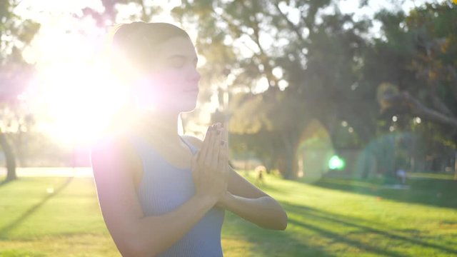 A beautiful young hispanic woman looking calm and relaxed in a prayer yoga pose during a meditation class in the park at sunrise.