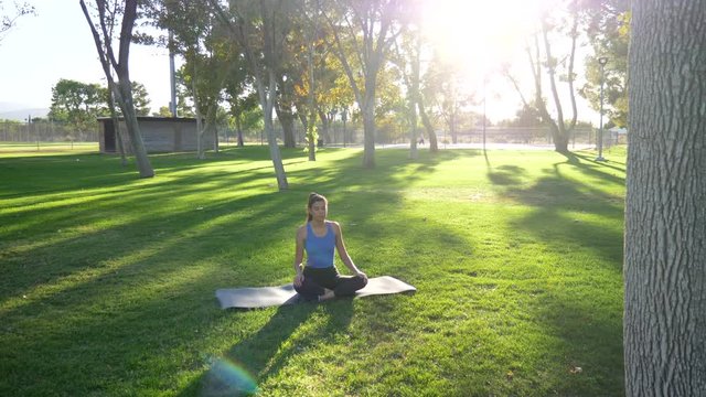 A beautiful young hispanic woman sitting and meditating for her mental health and anxiety in nature at sunrise.