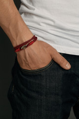 Close-up shot of a male wrist with a red leather multilayer bracelet made of braided cords with a...