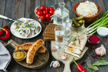 Vodka with lard, salted fish and vegetables, sausages on wooden background. Alcohol pure craft drink and traditional snack, tomatos, cabbage, cucumbers. Negative space. Celebrating food and delicious.