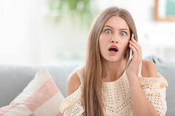 Surprised young woman talking by mobile phone at home