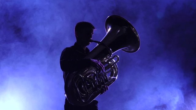 Musician in smoky studio playing in tuba, silhouette. Slow motion