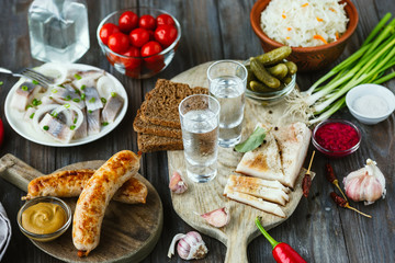 Fototapeta na wymiar Vodka with lard, salted fish and vegetables, sausages on wooden background. Alcohol pure craft drink and traditional snack, tomatos, cabbage, cucumbers. Negative space. Celebrating food and delicious.