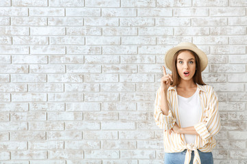 Surprised young woman with raised index finger against brick wall