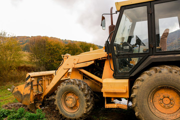 Tractor in the forest in autumn. Transport for repair work. Yellow tractor on green grass