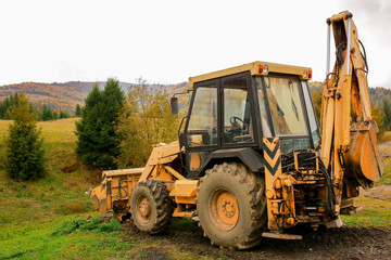 Fototapeta na wymiar Tractor in the forest in autumn. Transport for repair work. Yellow tractor on green grass