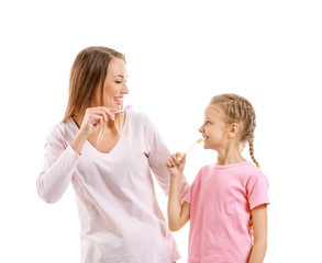 Portrait of mother and her little daughter brushing teeth on white background
