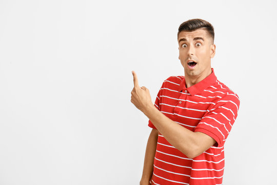 Surprised young man pointing at something on light background