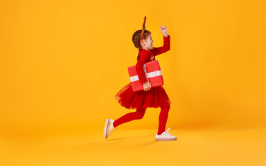 Fototapeta na wymiar happy funny child girl in red running with Christmas gift on yellow background.