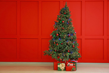 Decorated Christmas tree and gifts near color wall