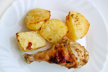 Appetizing baked chicken leg with potatoes on a white dish. Selective focus.