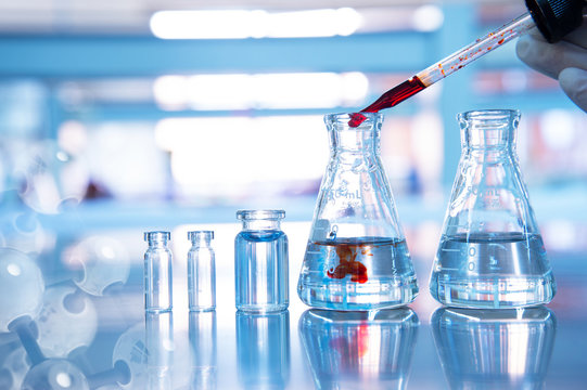 orange drop in glass flask with vial and chemical molecular on blue science laboratory background